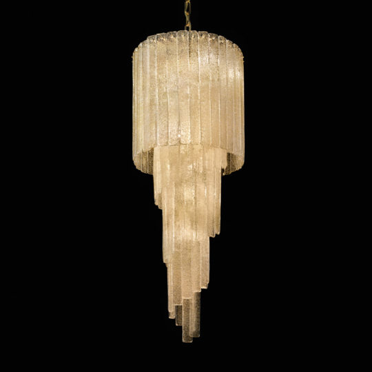 The Luxury Tiered Amber Glass Chandelier features multiple tiers of elongated, amber glass tubes cascading downward. It emits a warm, soft glow against a black background, highlighting its intricate design and opulent appearance.