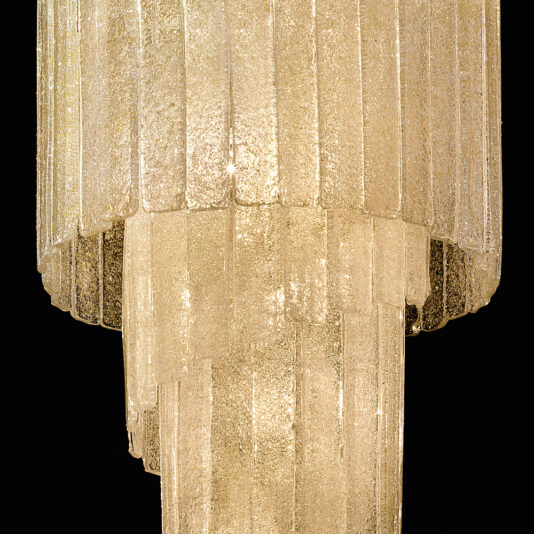 A close-up view of the Luxury Tiered Amber Glass Chandelier showcases its multiple tiers of elongated, textured amber glass prisms that emit a warm, golden light against a black background. The arrangement creates a cascading effect with a sophisticated, elegant appearance.