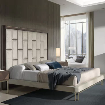 Luxury Velvet Fabric Upholstered Bed Modern bedroom with a Luxury Velvet Fabric Upholstered Bed showcasing a beige tufted headboard. The bed is dressed in gray and white bedding, complemented by a dark blue throw blanket. On either side of the bed are two bedside tables, each adorned with lamps. A large window in the background frames a view of trees and bathes the room in natural light.