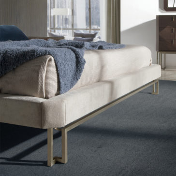 Luxury Velvet Fabric Upholstered Bed A close-up of a modern bedroom featuring the Luxury Velvet Fabric Upholstered Bed adorned with a soft blue blanket draped over it. The bed is situated on a plush, dark gray carpet. In the background, there is a window with sheer curtains and a wooden dresser featuring both a drawer and cabinet.
