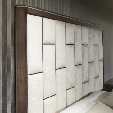 Luxury Velvet Fabric Upholstered Bed The Luxury Velvet Fabric Upholstered Bed boasts a large, modern headboard with a geometric, padded design featuring rectangular panels of light gray velvet upholstery framed with dark wood. Set against a wall with a textured finish, this bed creates a sophisticated and stylish bedroom aesthetic.