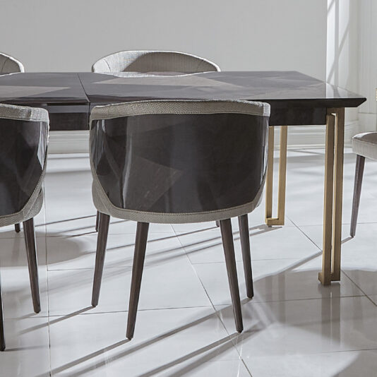 Luxury Veneer And Brass Extendable Dining Table A contemporary dining room ensemble features a Luxury Veneer and Brass Extendable Dining Table, accompanied by four elegant gray upholstered chairs with wooden legs. The set is beautifully arranged on a light-colored tiled floor, where sunlight pours in, creating dynamic shadows across the space.