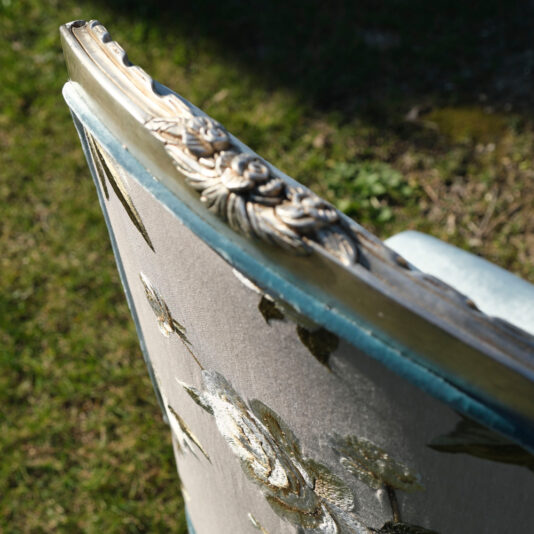 Close-up of the Luxury Venetian Style Occasional Chair, featuring an ornately carved wooden frame with intricate floral designs. The upholstery boasts embroidered flowers in shades of green and white. The chair is placed outdoors on a grassy surface.