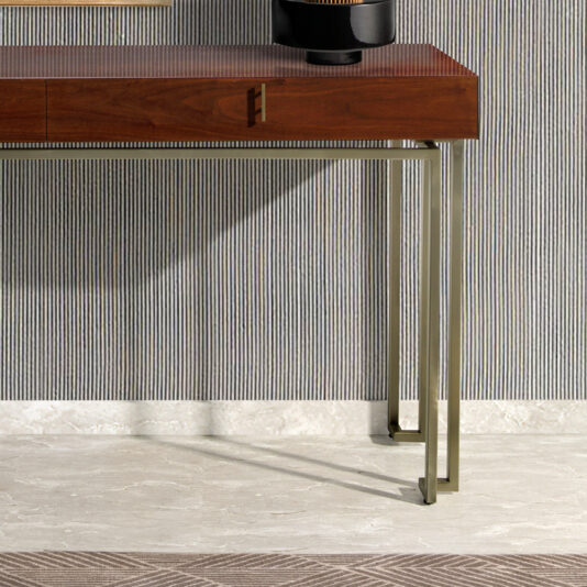 A Luxury Walnut Veneer Console Table with sleek metal legs sits against a vertically striped wallpaper. A decorative piece is partially visible on the far side of the table. The flooring is light-colored stone with a patterned rug at the bottom edge.