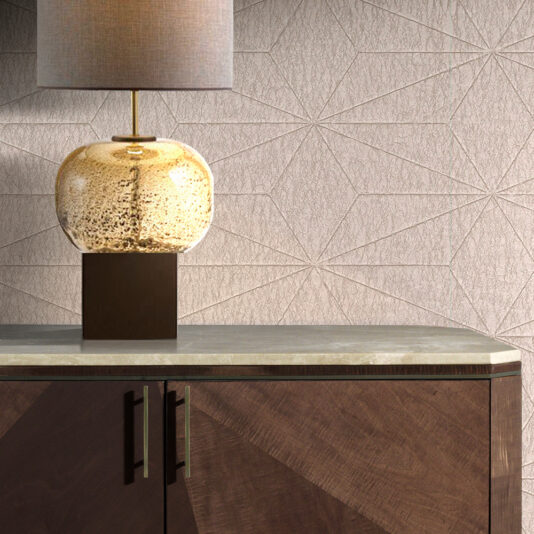 Marble Top Brown Maple Sideboard A table lamp with a textured beige shade and a round, speckled glass base sits atop the Marble Top Brown Maple Sideboard, which boasts modern geometric detailing and metallic handles. The backdrop highlights a wall adorned with a geometric pattern.