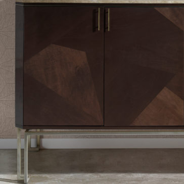 The Marble Top Brown Maple Sideboard is a modern wooden cabinet featuring a marble top and geometric patterns on its doors. This sideboard has two brown maple doors with metal handles and stands on slim metal legs. It is showcased against a textured wall with hexagonal patterns and placed on a smooth, light-colored floor.