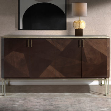 The Marble Top Brown Maple Sideboard, featuring dark wooden geometric paneling and sleek silver legs, stands against a textured wall. A modern table lamp adorns its marble top, while a framed abstract art piece hangs above it.