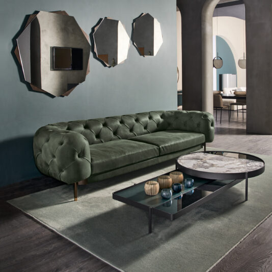 Modern Glass And Marble Modular Coffee Table A modern living room features a green tufted sofa and the Modern Glass And Marble Modular Coffee Table adorned with decorative vases. Three geometric mirrors on a blue wall add stylish flair, while dark wood floors and a light green rug complete the aesthetic. Arched doorways lead to other rooms.