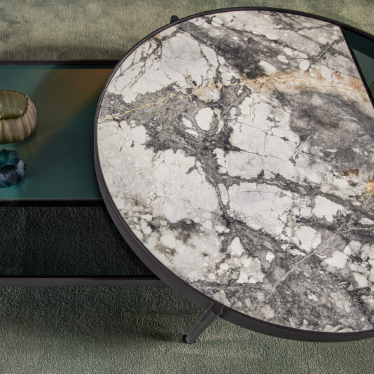 Modern Glass And Marble Modular Coffee Table The Modern Glass And Marble Modular Coffee Table showcases a large round segment with a cracked marble top and an opaque black-finished rectangular glass section. A textured green object adorns the table, which is placed on a soft green carpet.
