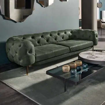 Modern Low Button Upholstered Suede Sofa A stylish living room features the Modern Low Button Upholstered Suede Sofa in plush green with rounded arms, positioned against a dark green wall. In front of the sofa is a sleek coffee table with a marble top and several decorative items on it, all placed on a grey rug over a dark wood floor.