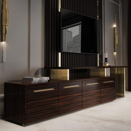 Modern Veneered TV Unit A modern living room features a sleek, dark wooden console table with four drawers, accented by gold-colored handles. Above it, a large flat-screen TV is mounted on a wall with vertical slats, seamlessly blending into the design of the Modern Veneered TV Unit. Minimalist sconces and a round mirror adorn the wall.