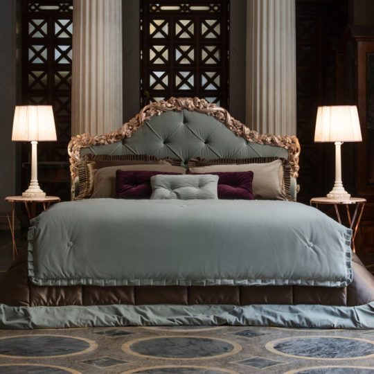 Luxurious bedroom featuring the Ornate Classic Style Button Upholstered Bed, adorned with teal bedding. The bed is accompanied by two elegant side tables with matching lamps, while tall classical pillars and intricate wooden panels in the backdrop add a touch of grand classic style.