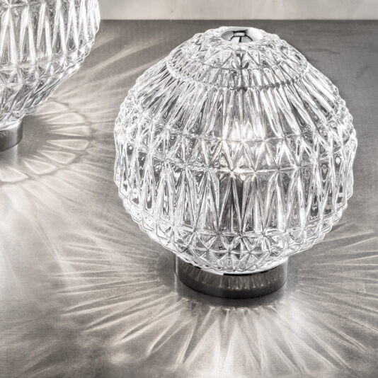Round Murano Glass Table Lamp Two intricately designed Round Murano Glass Table Lamps illuminate a surface. Their diamond patterns cast striking light and shadow effects on the metallic background, creating a visually appealing texture.