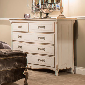 Tall Classic Louis Style Chest Of Drawers The Tall Classic Louis Style Chest Of Drawers is elegantly showcased in a room setting, featuring four larger drawers and two smaller top drawers adorned with ornate handles. This vintage-style dresser boasts decorative carvings and sits atop scroll feet. The top of the chest is beautifully decorated with items including a tall candelabra and a mirror.