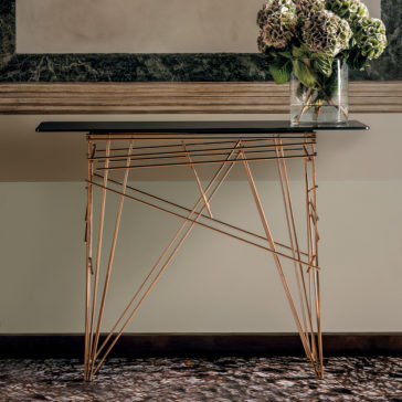 Contemporary Glass Console Table A Contemporary Glass Console Table featuring a sleek black glass top and an intricate geometric gold metal base is positioned against a wall. Atop the table sits a glass vase filled with green and purple hydrangeas, infusing the space with an elegant touch.