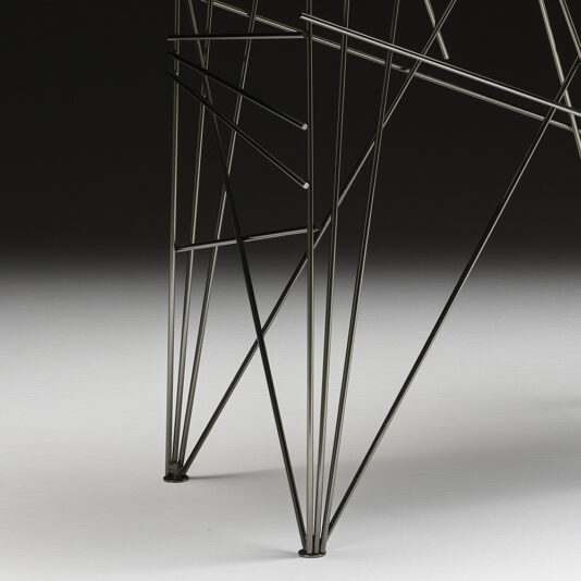 Close-up photograph of part of a metal wireframe structure, featuring thin intersecting rods forming geometric patterns. The Contemporary Lacquered Console Table stands on a smooth, light-colored surface against a dark background, creating a striking contrast.