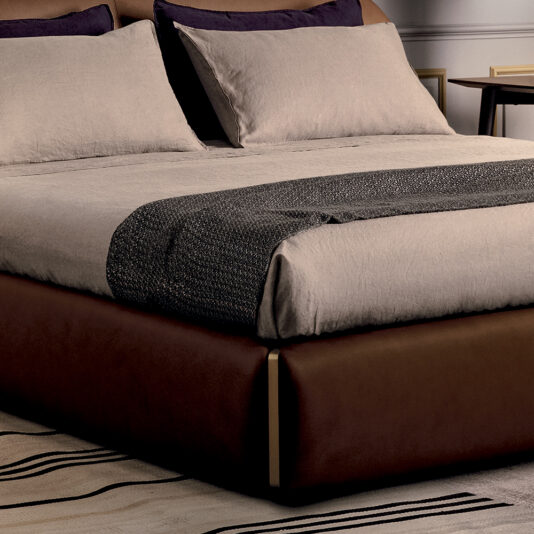 The modern bedroom is dominated by the Contemporary Leather Upholstered Curved Bed, neatly made with beige linens and dark gray accents. Pillow shams perfectly match the beige linens, while a textured gray throw is elegantly laid across the foot of the bed. Adjacent to it, a wooden nightstand holds a framed picture and table lamp.