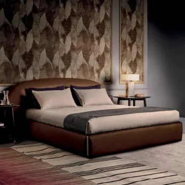 Contemporary Leather Upholstered Curved Bed A contemporary bedroom featuring the Contemporary Leather Upholstered Curved Bed, elegantly dressed in beige and gray bedding. It is flanked by two round wooden nightstands, each topped with a lamp. The walls are adorned with large framed botanical artwork, and a striped rug lies beneath the bed on the floor.