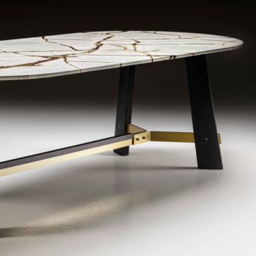 A close-up of the corner of the Contemporary Oval Quartz Dining Table, featuring an elegantly crafted white quartz surface accented with brown veining. The table is supported by sleek black angled legs and a stylish gold-colored metal crossbar for added stability. This modern piece stands out against a gradient background of dark to light gray.