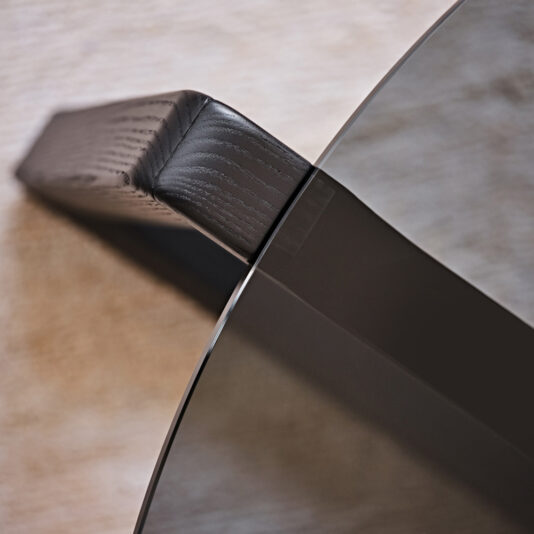 Contemporary Low Round Glass Coffee Table Close-up view of the Contemporary Low Round Glass Coffee Table, highlighting the intersection where its textured wooden leg meets the clear glass surface. The contrast between the wooden texture and sleek glass emphasizes its modern design aesthetics.