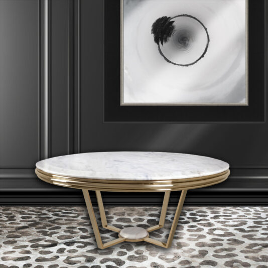 A modern room showcasing a **Contemporary Round Marble Coffee Table** with gold trim and angular gold legs, beautifully placed on a leopard-print rug. The black wall behind the table features a monochromatic abstract painting with a circular design.