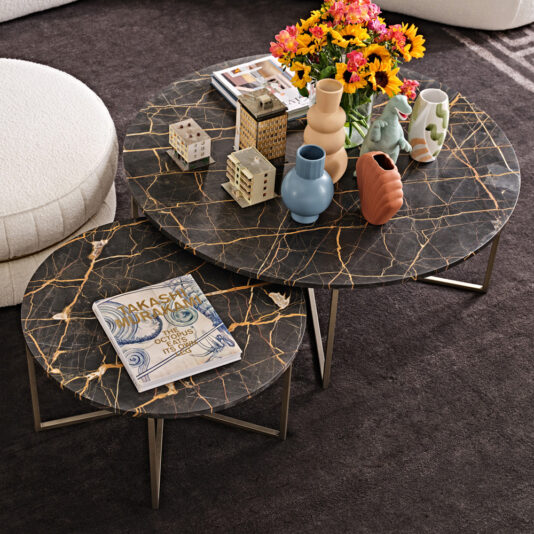 The Contemporary Round Marble Coffee Table Set displays ceramic vases, decorative house accents, a floral bouquet, and a magazine atop a dark rug next to a white curved sofa.
