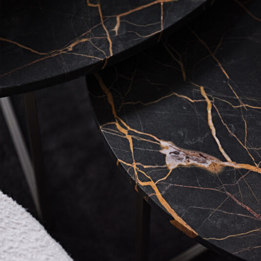 A close-up view of a dark marble surface with intricate golden-orange veins against a black background forming a striking natural pattern. The polished edges and shadows suggest the Contemporary Round Marble Coffee Table Set, with a white textured object partially visible in the corner.