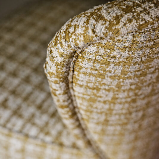 Contemporary Upholstered Occasional Chair Close-up view of the armrest on the Contemporary Upholstered Occasional Chair, which features a textured mustard-yellow and cream color scheme. The woven, patterned fabric accentuates the intricate detailing and craftsmanship of this contemporary chair.
