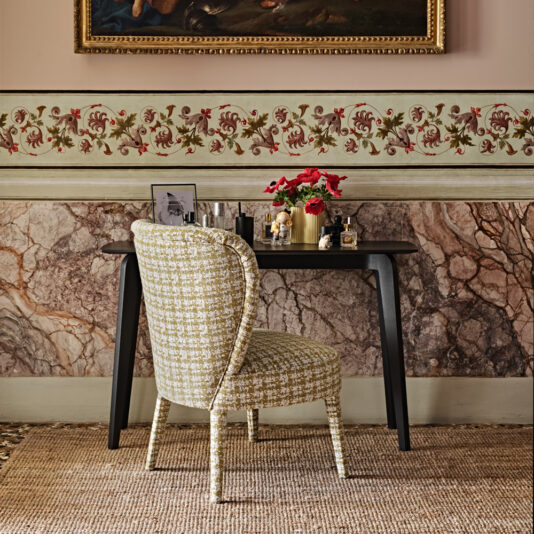 Contemporary Upholstered Occasional Chair A marble-textured wall, classic wooden desk with red flowers, a small photo, decorative items, and a painting create a stylish interior. Completing the look is a houndstooth-patterned Contemporary Upholstered Occasional Chair.