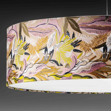 The Elegant Suspension Light With Embroidered Shade features a hanging cylindrical lampshade adorned with a colorful floral and botanical pattern in shades of pink, yellow, green, and white against a dark background. The interior is white, and it is elegantly suspended from the ceiling by thin wires.