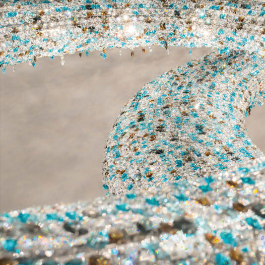 Luxury Coloured Crystal Chandelier A close-up image of an abstract sculpture adorned with sparkling blue, gold, and clear crystals. The intricate, twisting form creates a visually captivating, shimmering pattern reminiscent of the **Luxury Coloured Crystal Chandelier** against a neutral background.