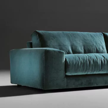 Luxury Large Velvet Modular Sofa A close-up photo of the Luxury Large Velvet Modular Sofa in a teal color against a dark gray background. This luxurious sofa showcases a plush, cushioned design with broad armrests and a soft, velvety texture. The image highlights one side of the large sofa, emphasizing its luxurious material and sleek lines.