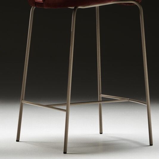 Luxury Mid Century Style Bar Stool The Luxury Mid Century Style Bar Stool features a dark seat with sleek, slender metal legs connected by a horizontal support bar. The image highlights the lower half of the stool against a dark background.