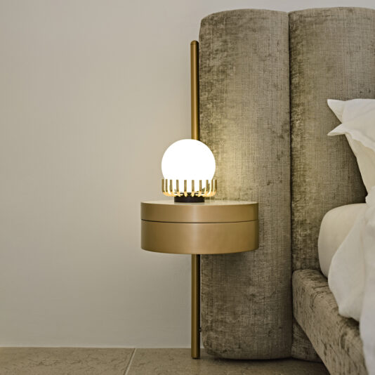 Luxury Modern Bed With Wide Headboard A modern bedroom boasts a luxurious Luxury Modern Bed With Wide Headboard in beige upholstery. Adjacent to it, a sleek, gold-colored wall-mounted bedside table adds sophistication. Atop the table, an elegant round lamp featuring a white globe and gold cage-like design bathes the space in warm lightācreating a truly opulent and modern sleeping environment.