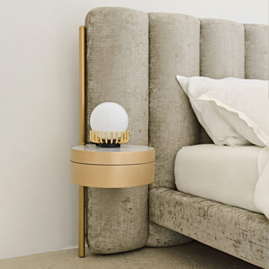 Luxury Modern Bed With Wide Headboard Introducing the Luxury Modern Bed With Wide Headboard, featuring a sophisticated beige upholstery and an attached tall, vertical gold rod. A chic, round gold-colored bedside table is affixed to the rod and comes complete with a spherical lamp boasting a gold base. The bed is adorned with pristine white pillows and bed linens for an elegant bedroom setup.