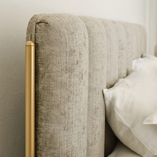 Luxury Modern Bed With Wide Headboard This Luxury Modern Bed With Wide Headboard displays a close-up of its beige, tufted headboard attached to a bed with white bedding. Elegant gold cylindrical accent posts adorn the edges, adding a touch of sophistication to the bedroom decor.