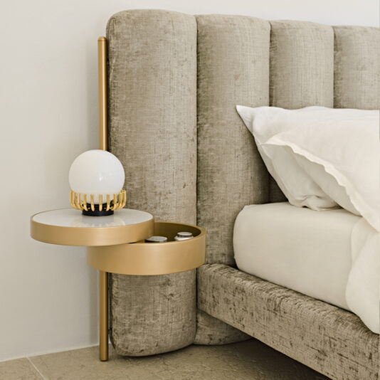 Luxury Modern Bed With Wide Headboard The Luxury Modern Bed With Wide Headboard creates a lavish bedroom scene with its plush, beige, velvet headboard. Attached to the expansive headboard is a chic gold-colored bedside table designed in a circular shape. The table supports a spherical white lamp and several small items, adding to the room's sophisticated ambiance.