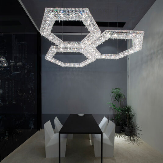 Luxury Octagonal Crystal Pendant Chandelier Modern dining room with a black table and four white chairs. Three Luxury Octagonal Crystal Pendant Chandeliers hang from the ceiling, casting a sophisticated light. A tall potted plant and a small spiky decorative plant are placed near the table.