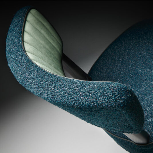 Modern Designer Dining Chair Close-up of the Modern Designer Dining Chair showcasing its textured teal fabric and sleek, curved design. The chair features a smooth green inner surface with black accents, creating a stylish and contemporary look against a neutral background.