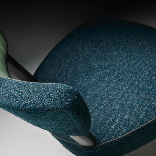Modern Designer Dining Chair Close-up of the Modern Designer Dining Chair's seat and partial backrest, covered in textured teal fabric. The chair features black legs and a slightly curved backrest, highlighting its sleek and contemporary design against a dark grey background.