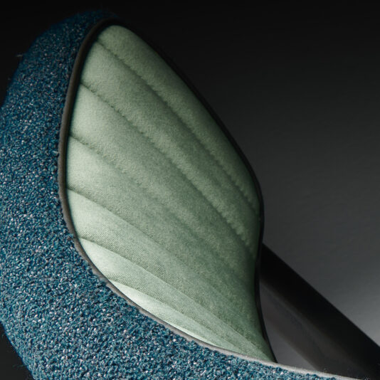 Modern Designer Dining Chair Close-up image of the Modern Designer Dining Chair, showcasing its textured blue-green fabric backrest and sleek quilted light green panels. The image highlights the intricate stitching and striking material contrasts.