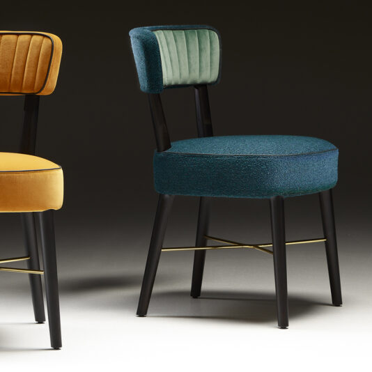 Modern Designer Dining Chair Modern Designer Dining Chair: This set includes two vibrant pieces, each equipped with sleek black legs and a brass crossbar support. One chair features a mustard yellow seat and backrest, while the other has a teal seat paired with a light green backrest. The backdrop is styled with a dark gradient for added sophistication.