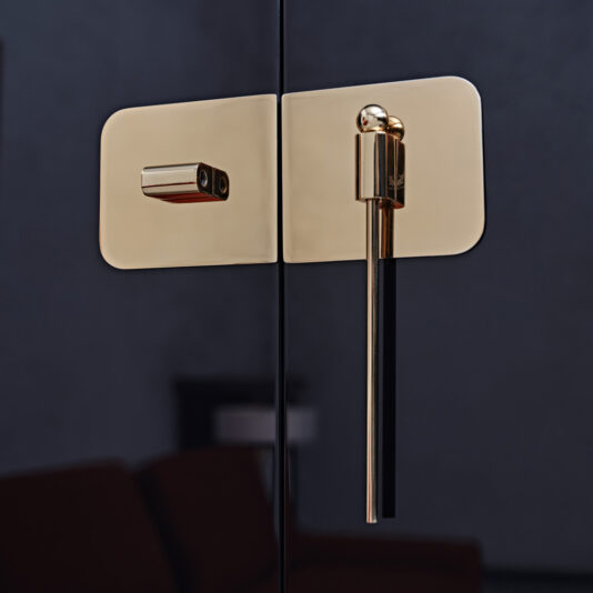 Close-up of an elegant, modern door handle with a sleek design, featuring gold and black components, reminiscent of the Modern Lacquered Cocktail Bar Cabinet. Set against a dark background, the polished finish gives it a sophisticated and contemporary look.