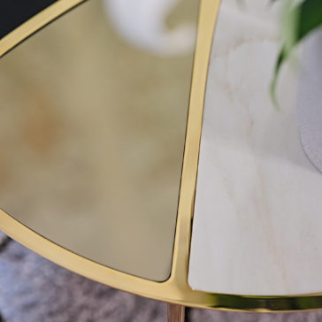 Close-up of the Modern Nest Of Coffee Tables, showcasing its unique segmented top. The table surface is elegantly divided into two sections: one side boasts a reflective gold surface while the other side displays a sophisticated white marble texture. A green plant is partially visible at the right edge of the image.