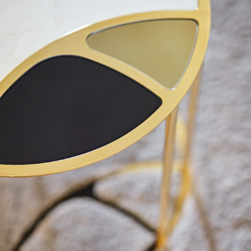 The Modern Nest Of Coffee Tables is a stylish and artistic set with oval tops showcasing three distinct color segments: black, gold, and white. Each table features a sleek gold frame and stands on slender gold legs, elegantly positioned on a textured, light-colored rug.