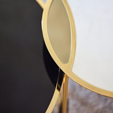 A close-up view of the Modern Nest Of Coffee Tables reveals a chic design: one table boasts a glossy black surface with a gold rim, while the other features a white surface with a gold rim. This combination creates an elegant contrast between the dark and light surfaces, accentuated by metallic touches.