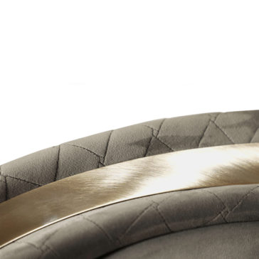 Close-up of a luxurious, quilted fabric featuring a geometric pattern, with an elegant, brushed gold metal accent running diagonally across. The cushioned fabric suggests it is part of the Modern Quilted Velvet Swivel Tub Chair.