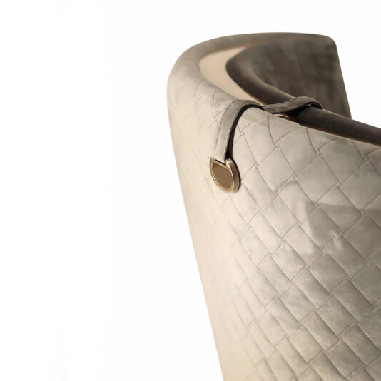 Modern Quilted Velvet Swivel Tub Chair A close-up view of the Modern Quilted Velvet Swivel Tub Chair showcases its luxurious quilted backrest crafted from light fabric, adorned with a decorative metal emblem on a leather strap hanging from its edge. The image emphasizes the chair's elegant texture and exquisite craftsmanship.