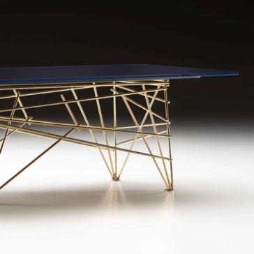 The Modern Rectangular Glass Coffee Table features a blue rectangular top and an intricate geometric gold metal base. Set against a dark background, the illuminated table stands out with its contemporary and artistic design.