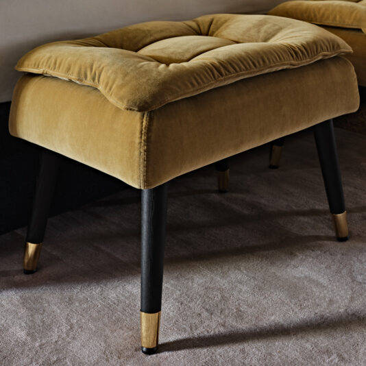 Small Button Upholstered Velvet Bench A plush small button upholstered velvet bench in mustard-yellow, featuring button-tufted cushioning, sits on four black wooden legs tipped with golden accents. The background reveals part of another identical bench, contributing to a sophisticated and cozy interior setting.